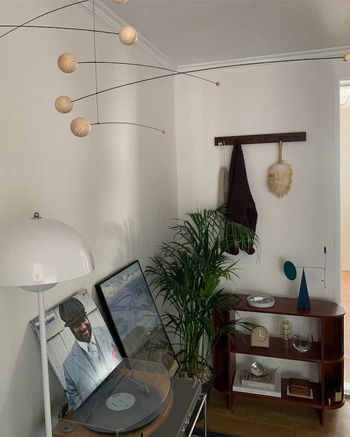 A living room with white walls and wood tone furniture, featuring a mobile and floor lamp that create a stylish, minimal natural atmosphere