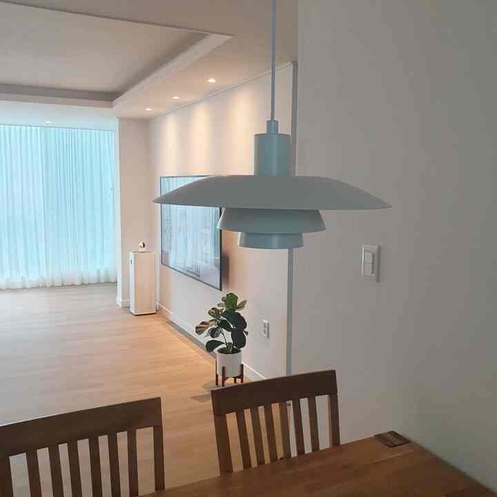 Minimal style living and dining room with dominant white and wood tones, featuring a pendant light and wooden dining chairs.