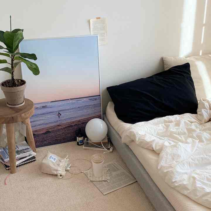 Light beige tone bedroom featuring a wood stool and large poster, creating a natural and modern space