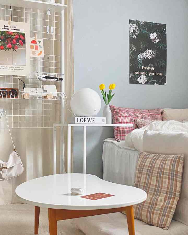 A compact living and bedroom space featuring white and beige tones, a floor cushion, and a white coffee table creating a cozy and clean atmosphere