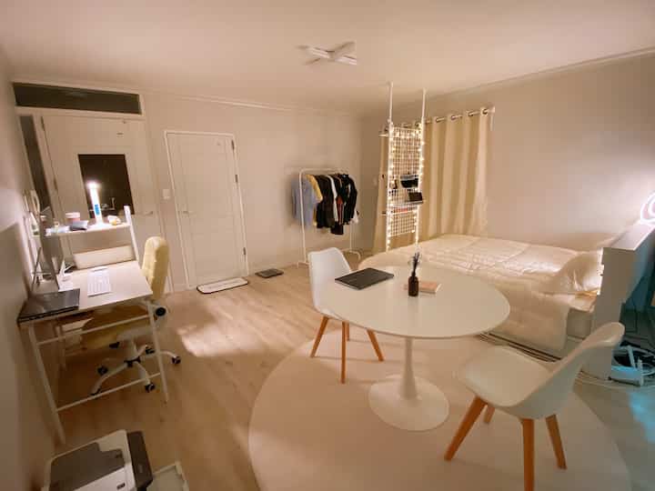 White and wood tone 6-pyeong studio apartment featuring bed, desk, and round dining table in a simple and clean single male household space