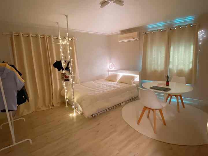 ホワイトとベージュのトーンが調和するワンルームの寝室、シンプルな家具と柔らかな照明のある落ち着いた空間