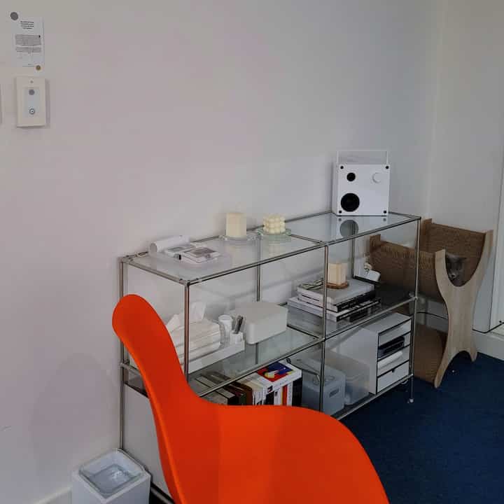 Minimal Mid-Century Modern living room with blue carpet and orange chair, featuring transparent modular shelves and candles in a calm setting