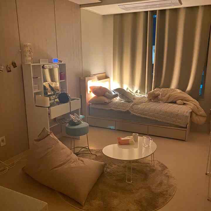 A cozy studio bedroom in soft beige tones featuring a bed, bean bag, and vanity arranged warmly