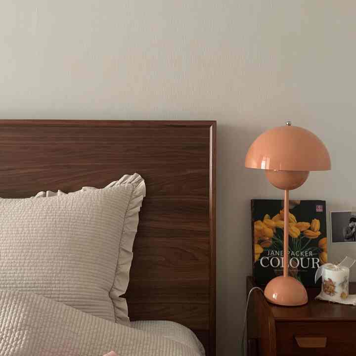 Cozy bedroom with soft beige quilted bedding on dark brown wooden bed frame, featuring a pink table lamp on adjacent nightstand