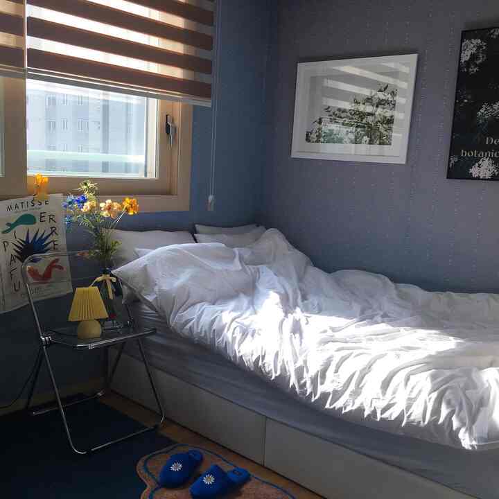 Bedroom with white bedding and transparent nightstand bathed in morning sunlight against blue wallpaper