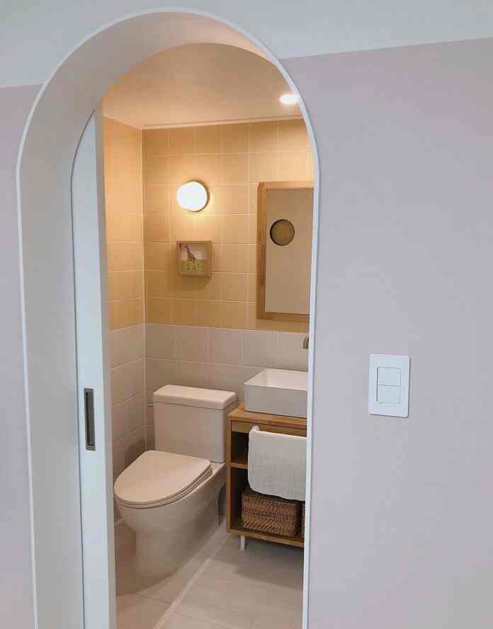 Beige and white toned bathroom featuring a toilet, sink, rattan basket, and picture frame with a clean atmosphere