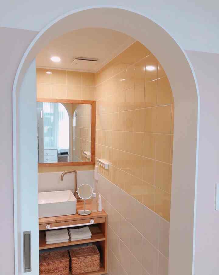 ナチュラルカラーと木目調のバスルーム、大きな木枠の鏡とラタンバスケットが配置された落ち着いた印象的な空間