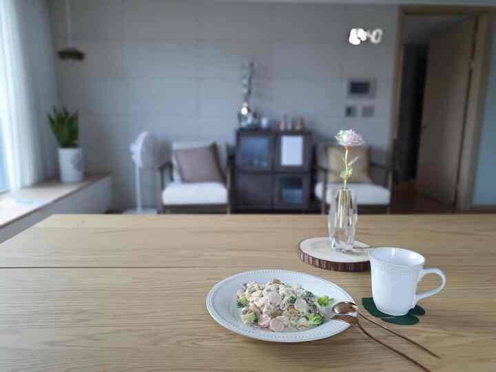 Bright natural wood tone living room featuring a central table with home cafe setup and rose vase, creating a simple atmosphere