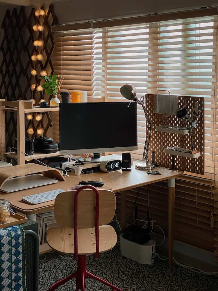 Wood tone home office featuring a monitor, desk lamp, and beige wood blinds creating a tidy workspace atmosphere