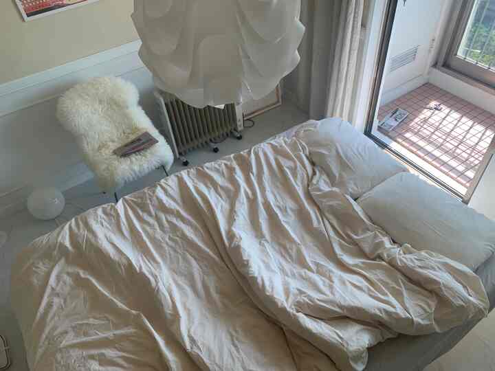 Bright white and beige bedroom with wooden bed frame, soft bedding, and open balcony door creating a cozy atmosphere