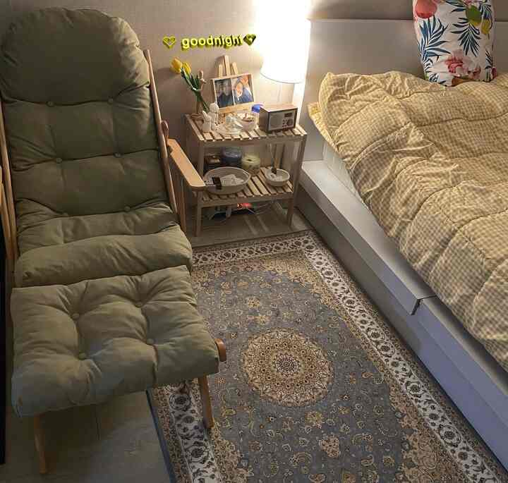 Natural and yellow toned studio bedroom featuring olive recliner armchair and Persian-style carpet with a cozy atmosphere