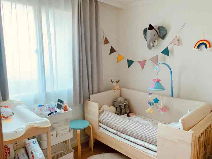 ベージュとナチュラルカラーの子供部屋、木製のベビーベッドとおむつ交換台、ガーランドが配置された温かみのある空間