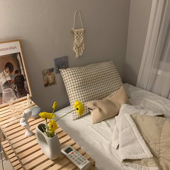 A cozy studio bedroom in warm beige and natural tones, featuring wooden shelves and bedding