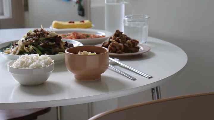 White-toned studio apartment dining space featuring a round table set with various Korean side dishes and bowls, conveying a clean and cozy atmosphere