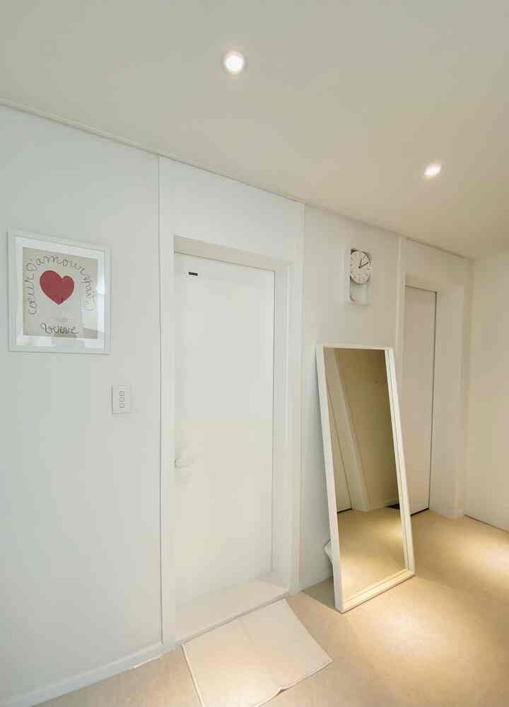 White-toned entrance space featuring minimalist minus molding, sliding door, wall clock, and a large mirror with a simple interior style