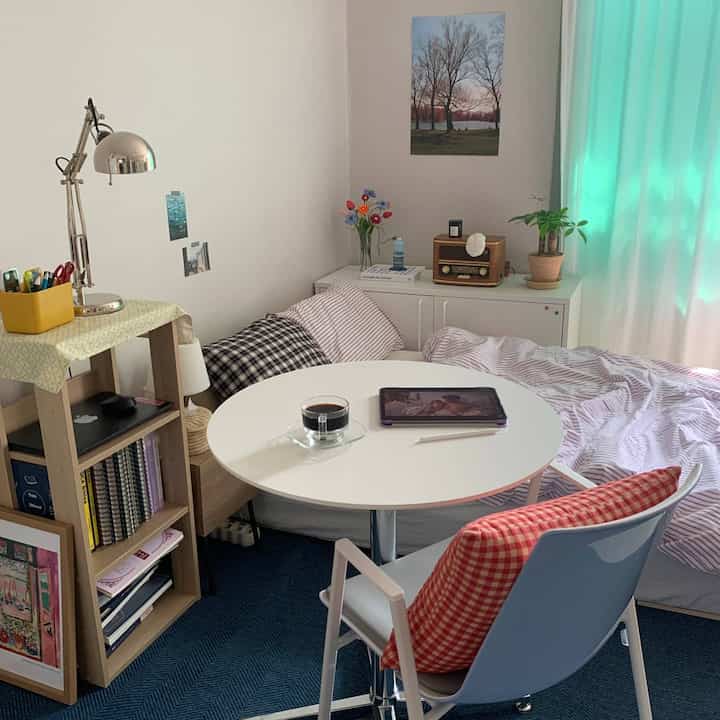 ナチュラルな色調のワンルーム寝室、白い円形テーブルとヴィンテージの小物が置かれた印象的な空間