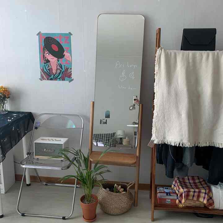 ナチュラルトーンのワンルーム、壁に大きな全身鏡と透明な椅子、木製のハンガーラック、観葉植物が配置された雰囲気のあるヴィンテージ風インテリア