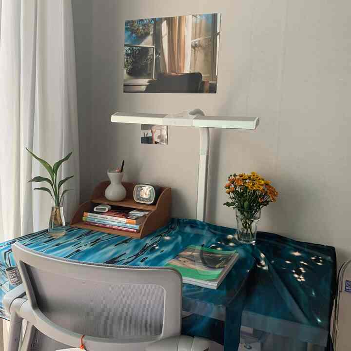 A studio apartment study space with white and wood tones, featuring an LED desk lamp and flower vases creating a cozy desk environment