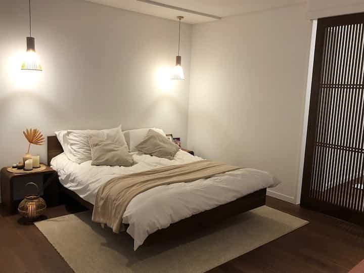 Natural wood tone bedroom featuring slatted door and pendant lights with a simple, warm atmosphere