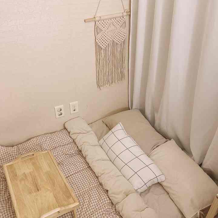 Natural wood tones and white curtains in a studio apartment space, featuring bedding and a macrame wall hanging for a cozy atmosphere