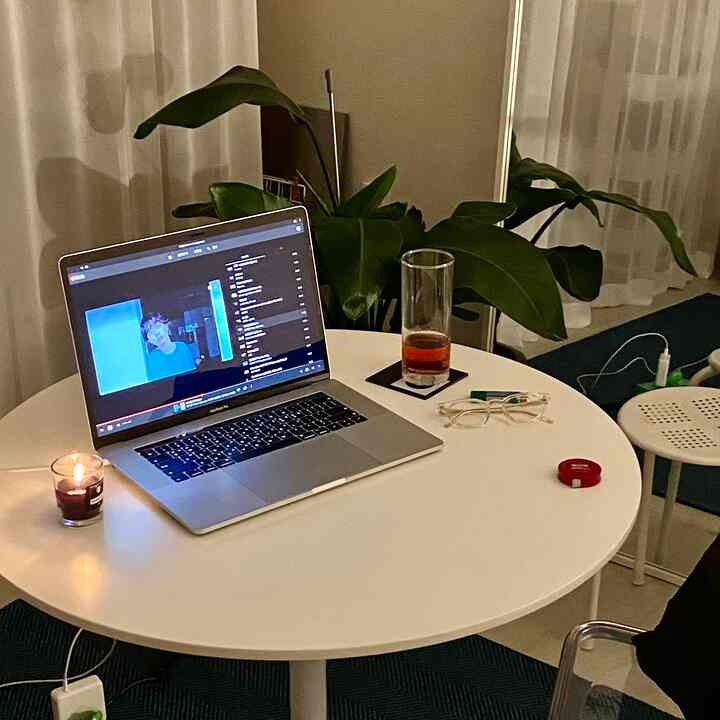 White-toned living and workspace featuring a round table with a laptop and candle, complemented by plant decor creating a cozy atmosphere