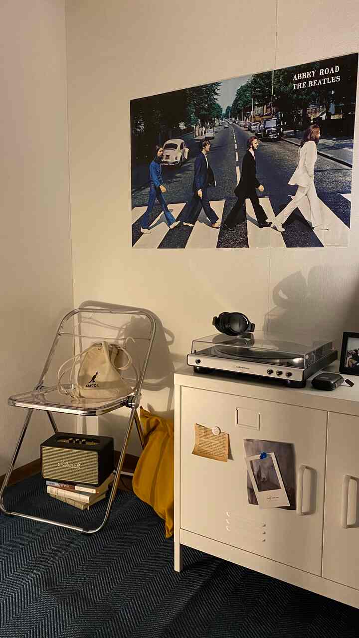 ブルーのヘリンボーンラグと透明な椅子、白いキャビネットの上にターンテーブル、壁にビートルズのポスターがあるレトロな雰囲気の空間