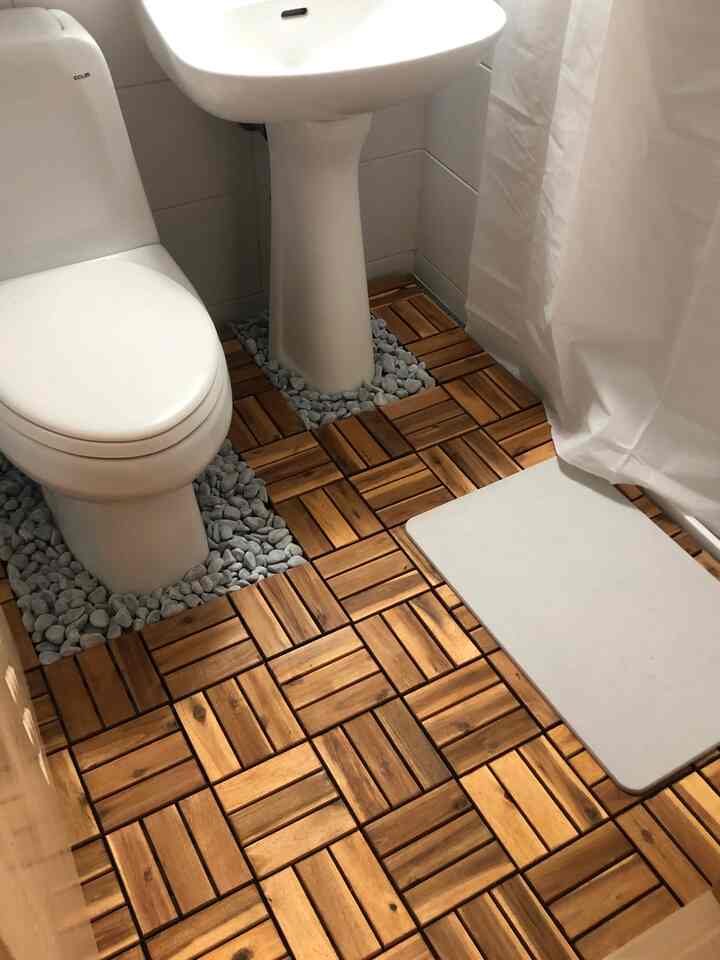 木目調のバスルーム、木製タイル床と白いトイレ、洗面台、カーテンが配置された清潔感のある空間