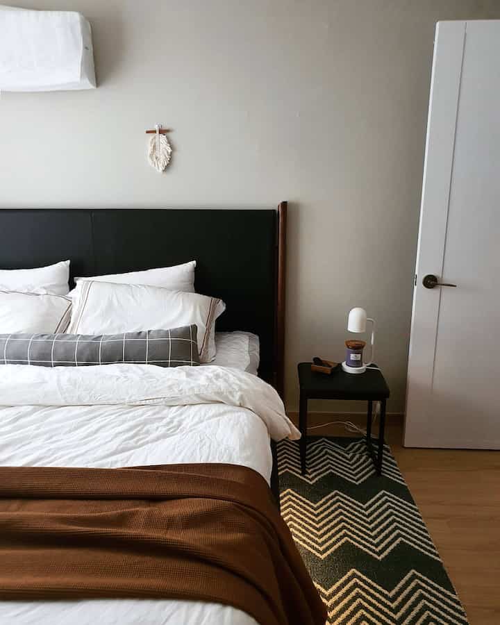 Modern bedroom in white and brown tones featuring a black headboard bed, nightstand, and patterned rug, creating a cozy autumn atmosphere