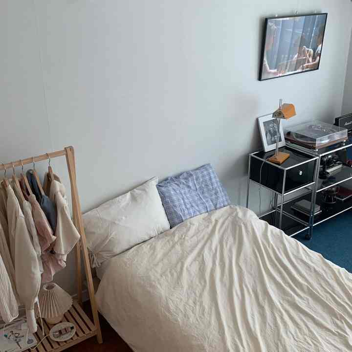 White-walled single bedroom with wood-tone clothes rack, simple and natural atmosphere