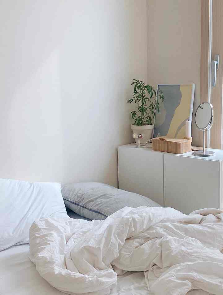 White and beige toned bedroom corner featuring white bedding and storage chest with a clean and cozy atmosphere