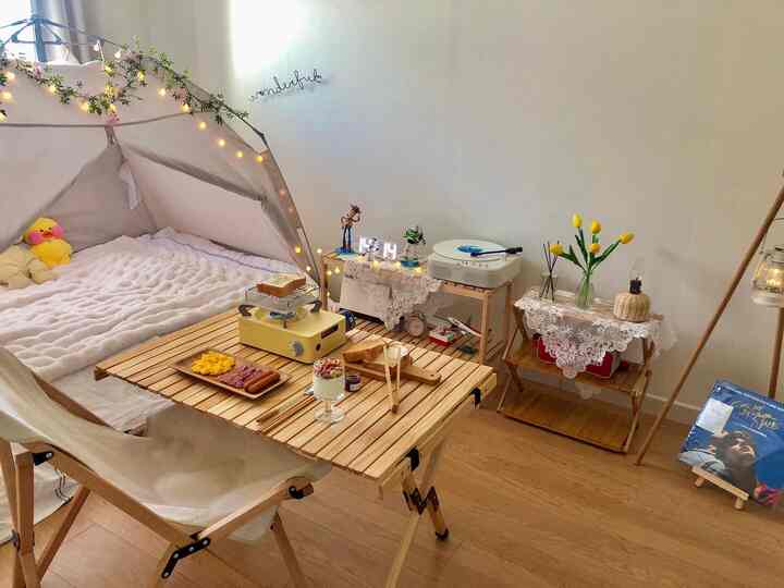 ナチュラルな木目調のワンルーム寝室、ホームキャンピングテントと折りたたみテーブルにホームカフェの料理が置かれた雰囲気のあるインテリア