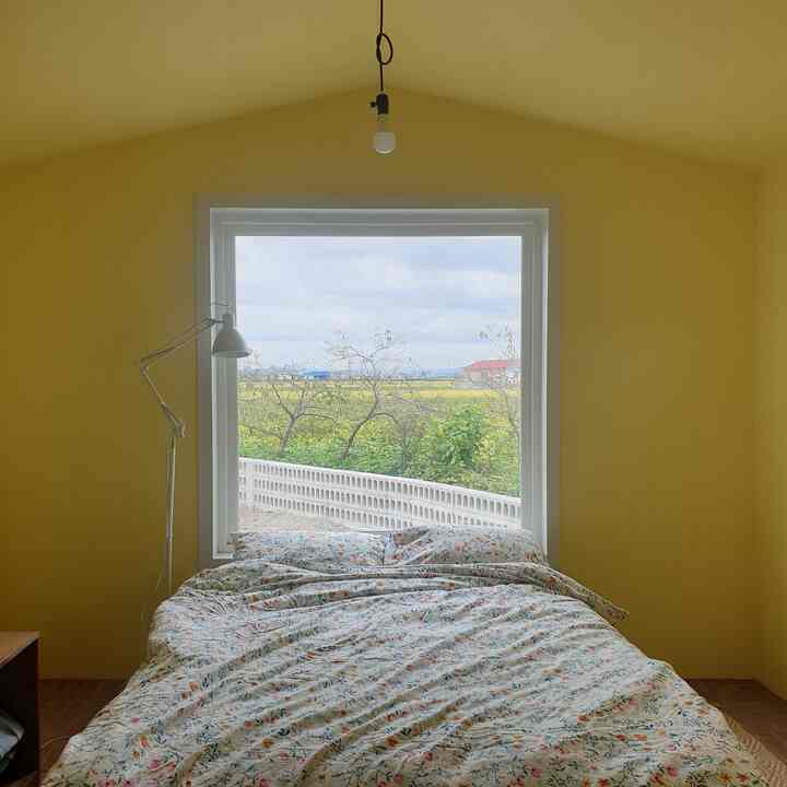 Yellow-toned bedroom featuring a large window, bed, and standing lamp with cozy atmosphere