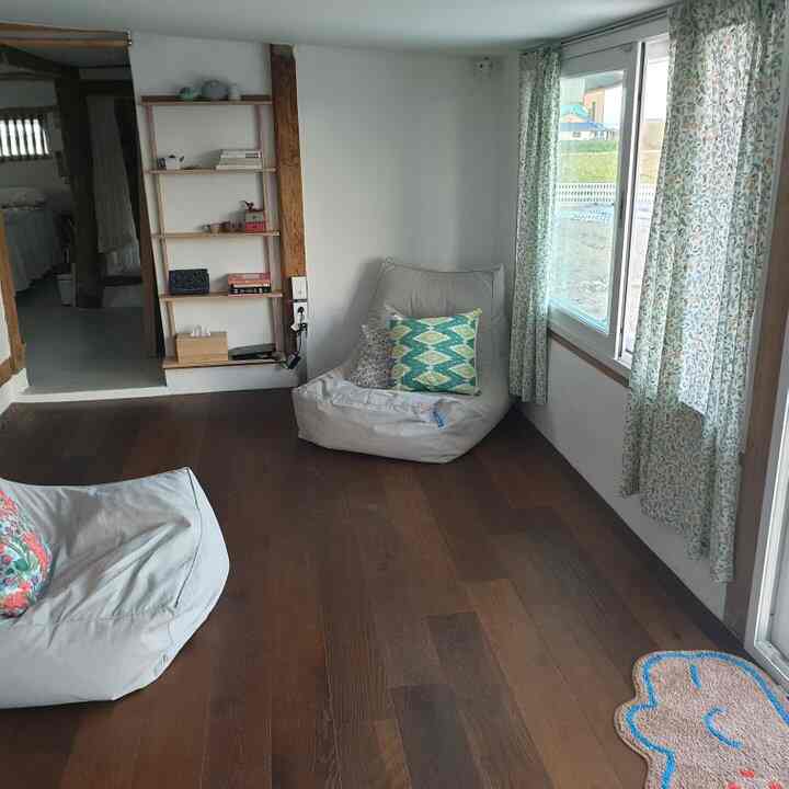Natural-toned living room with wood flooring, white walls, two bean bag chairs, and floral curtains creating a cozy atmosphere