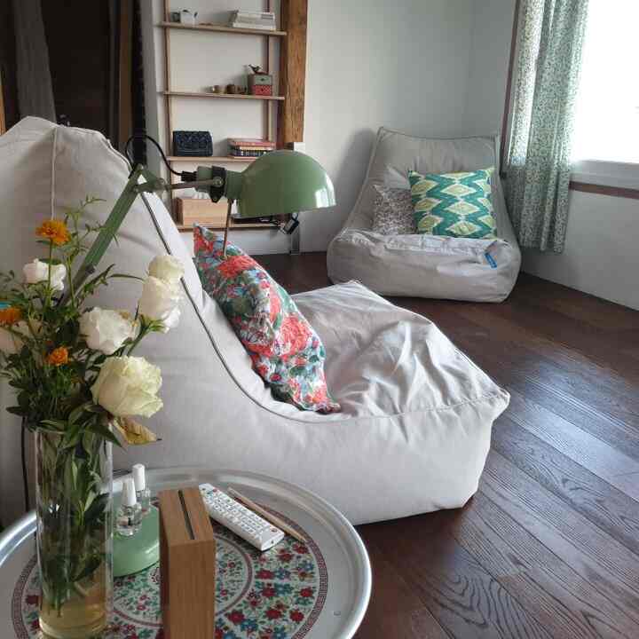 White-toned living room with natural wood flooring, featuring bean bag sofas and a floor lamp creating a cozy atmosphere
