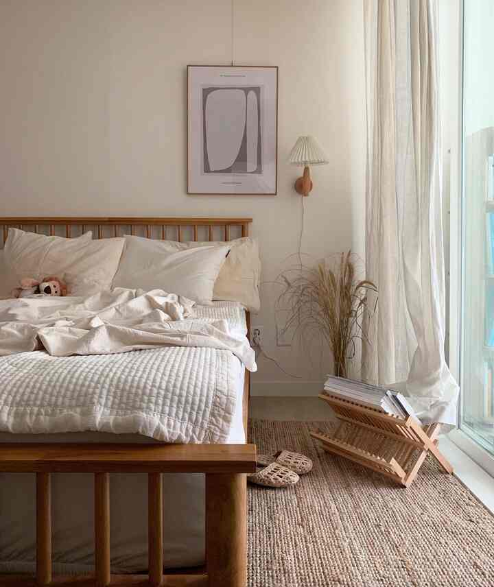 ナチュラルな色調の寝室、木製ベッド、リネンカーテン、ラタンラグが配置され、温かみのある落ち着いた雰囲気のインテリア