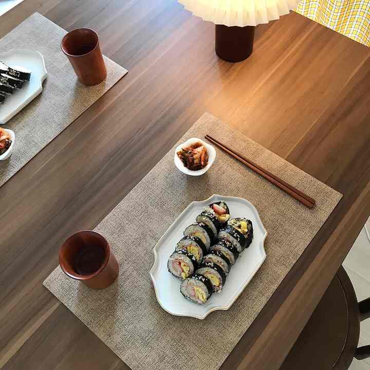 Warm wood-toned Morini table in living room with placemats and kimbap, creating a cozy home cafe atmosphere
