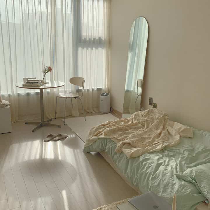 Bright studio bedroom in white and mint tones featuring simple furniture and soft natural light.