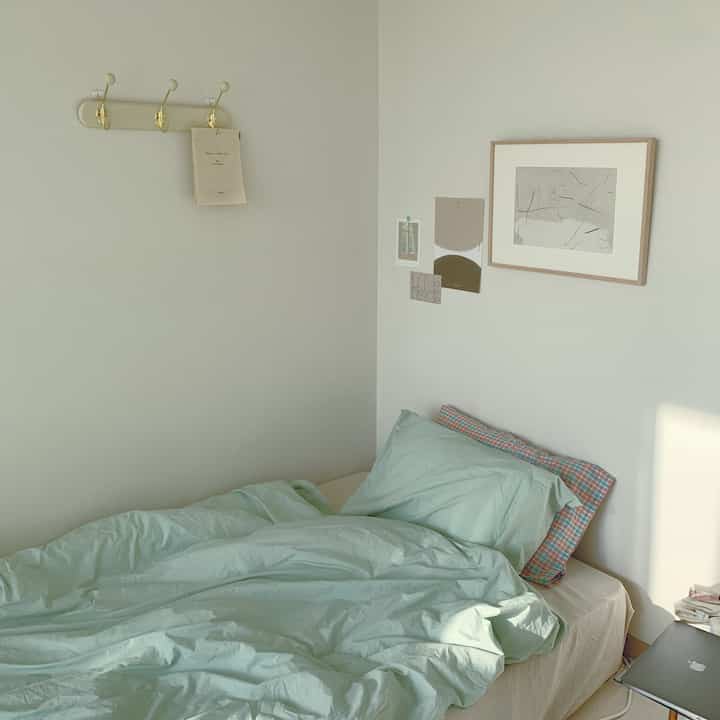 Soft natural-toned bedroom featuring light green bedding and simple wall art creating a cozy atmosphere
