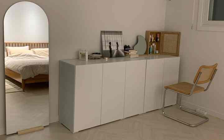 White and wood tone bedroom space featuring large full-length mirror and minimalist storage cabinet in simple modern style
