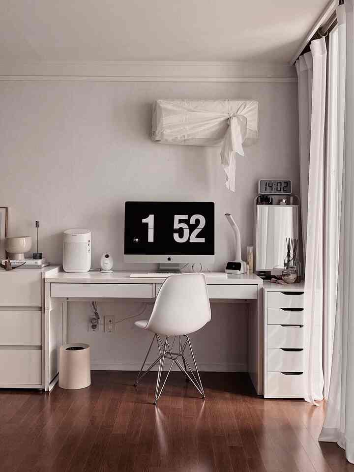 White and wood-tone study featuring a clean desk, chair, and digital clocks in a simple home office space