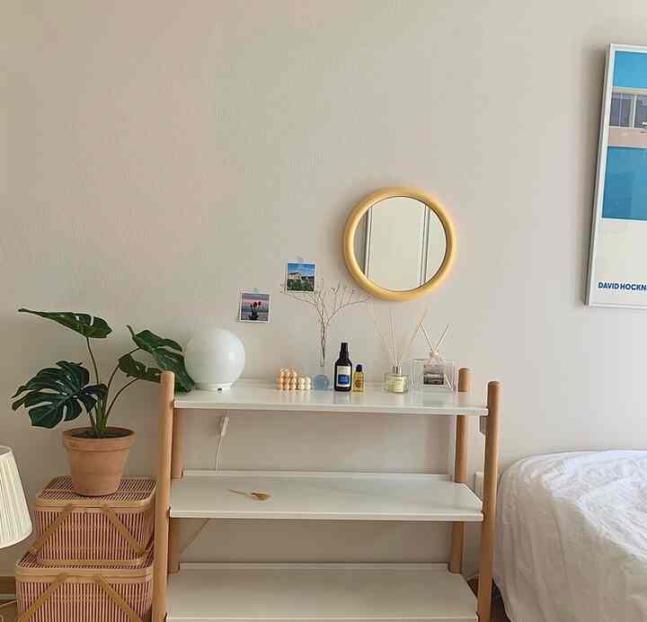 ベージュの壁と木製の棚、丸い鏡、植物が配置された自然で落ち着いた寝室のインテリア