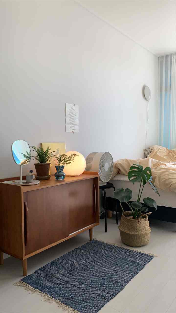 ベージュ色調の寝室、木製の収納キャビネットと植物が配置された、落ち着いた自然な雰囲気のインテリア