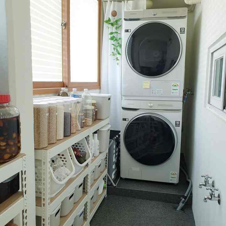 White and gray toned narrow, long laundry room featuring stacked washer and dryer with organized shelving and containers