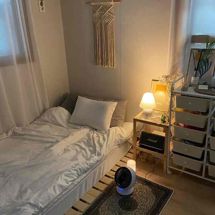 Cozy studio bedroom in warm beige and wood tones featuring mattress, nightstand, and macrame wall hanging