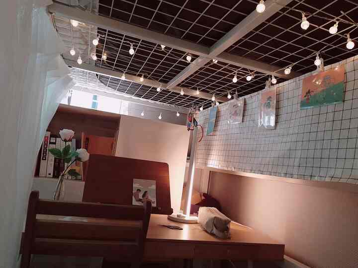 白と木目調の狭い部屋にデスクと棚、ストリングライトとテーブルランプが配置された雰囲気のある学習空間