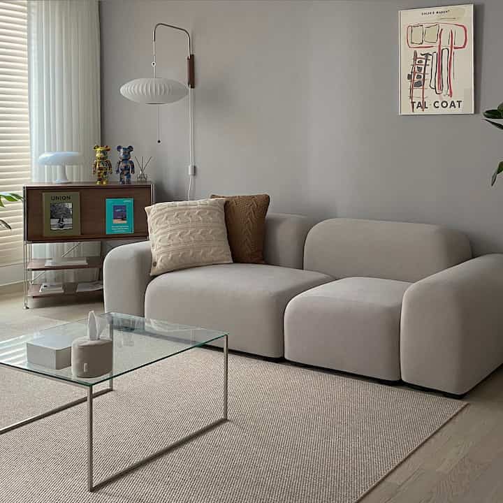 Beige natural modern living room featuring large sectional sofa, glass coffee table, wall sconce, and wood furniture in a clean setting