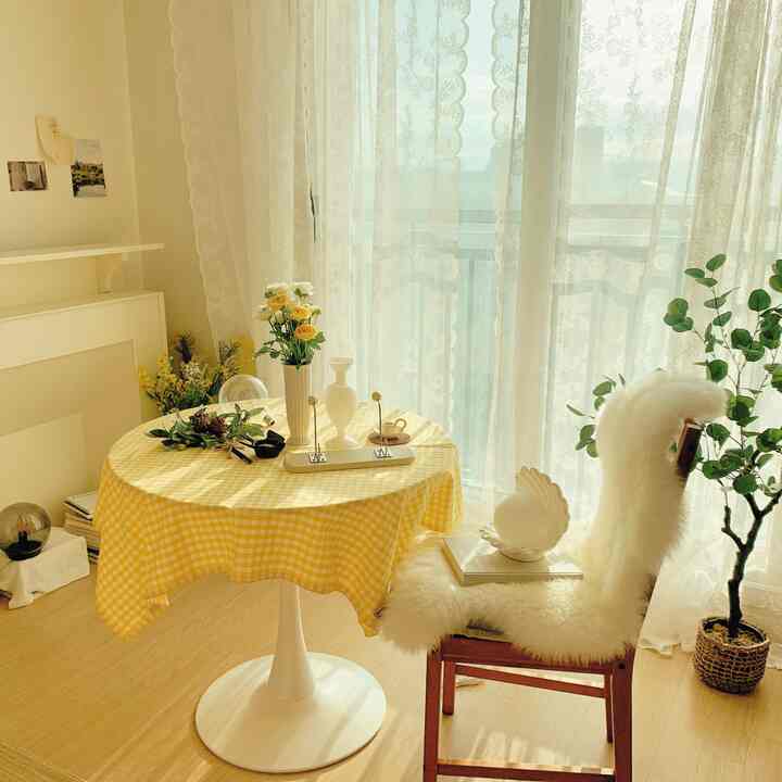 A natural modern living room space featuring a round table with yellow check tablecloth and lace curtains with bright white tones
