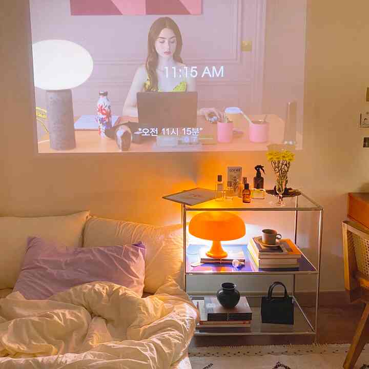 A white and orange-lit studio bedroom featuring a home cinema setup and home office elements creating a cozy atmosphere