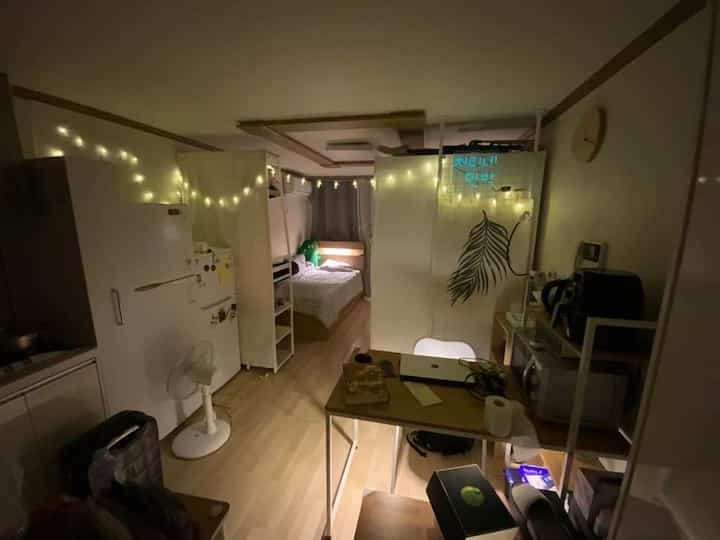 白と温かみのある木目調が調和するワンルーム、狭いレイアウトにベッドやダイニングテーブル、収納が配置された居心地の良い一人暮らし向けのインテリア